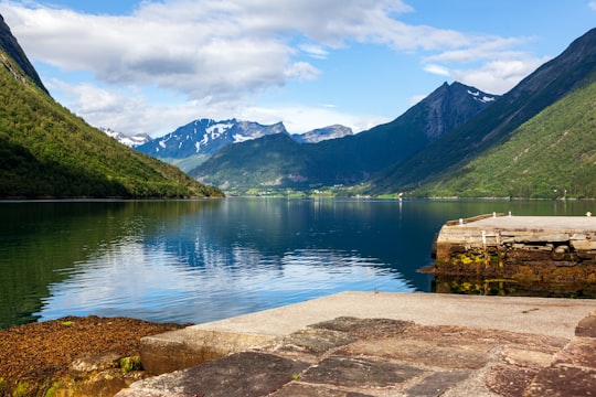 brown wooden house near lake under blue sky during daytime in Hjørundfjorden Norway