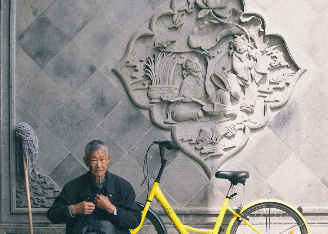 man in black jacket sitting beside yellow bicycle
