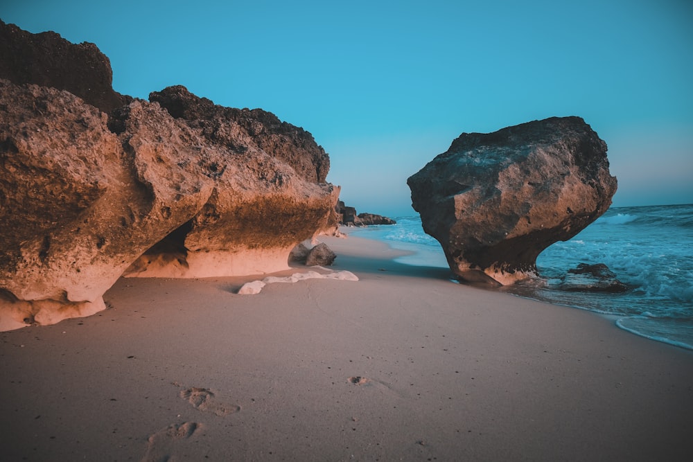 brown rock formation on white sand beach during daytime