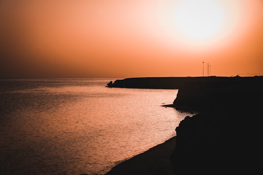 silhouette of person standing on rock formation near body of water during sunset in Kish Iran