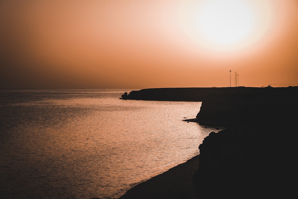 Silhouette einer Person, die während des Sonnenuntergangs auf einer Felsformation in der Nähe eines Gewässers steht