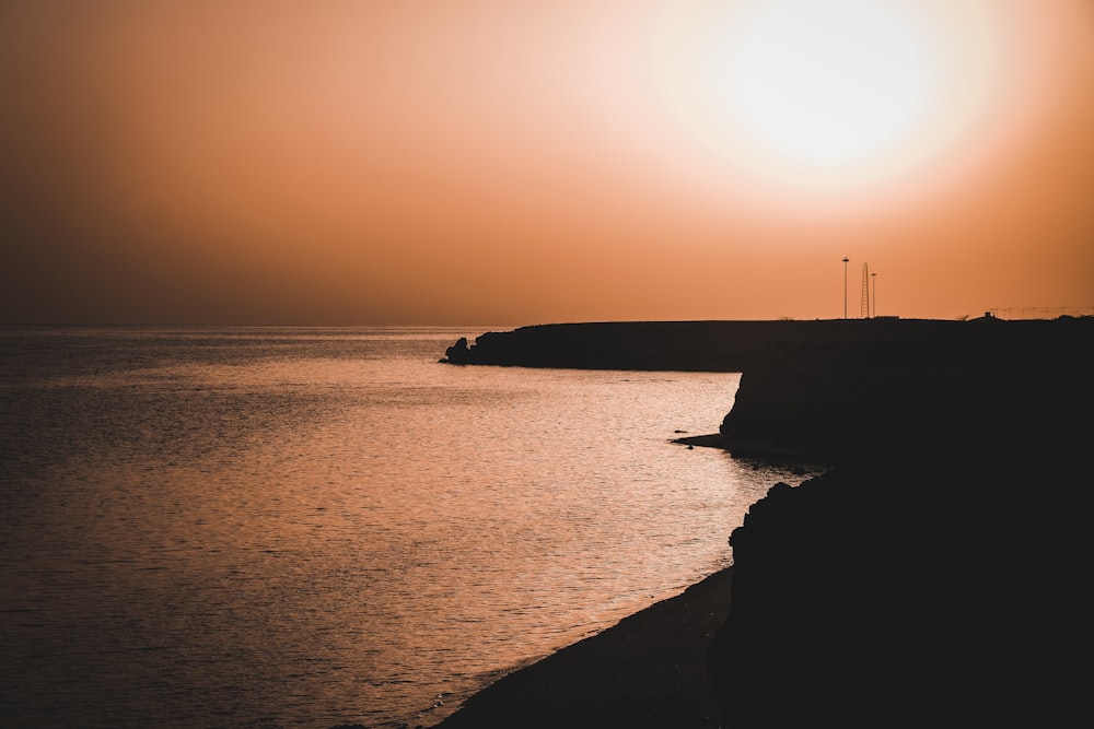 silhouette of person standing on rock formation near body of water during sunset