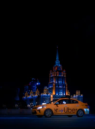 An Uber car glowing under streetlights with illuminated ads on its windows during nighttime.