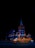 A brightly illuminated building at night with an orange and black Uber taxi in the foreground. The building features elaborate architectural details and is lit with blue and orange lighting, creating a striking contrast against the dark sky.