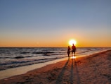 A couple holding hands while walking on a beach.
