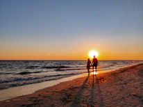 A couple walking hand in hand along a quiet beach at sunset.