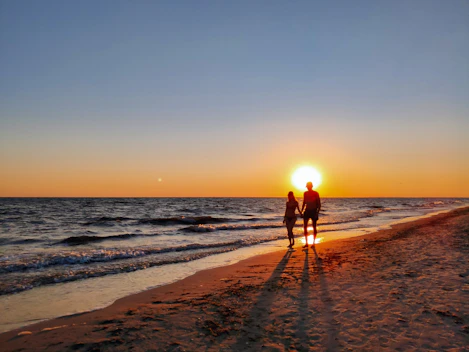 A couple walking hand-in-hand along a pristine white sandy beach at sunset.