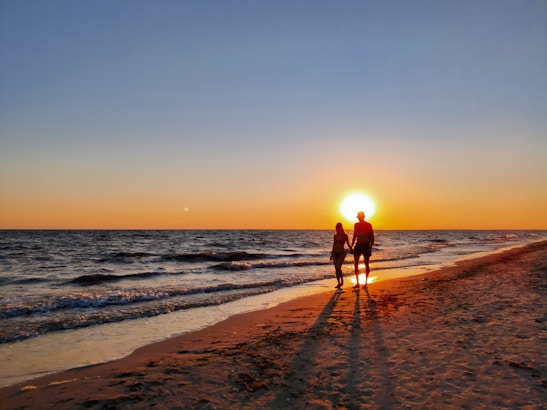 A romantic couple walking hand-in-hand along a picturesque shoreline at sunset.