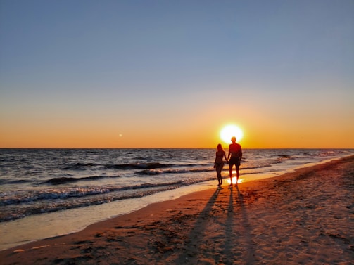 A couple walking hand in hand on a scenic beach at sunset.