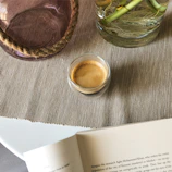 An espresso cup resting on a linen napkin beside an open book with warm neutral tones.