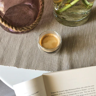 A minimalist espresso cup resting on a textured linen napkin beside an open book.