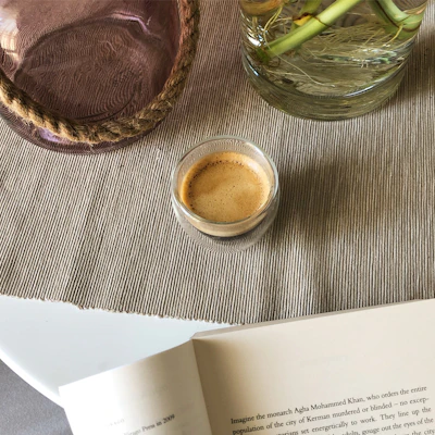 An espresso cup resting on a linen napkin beside an open book with warm neutral tones.