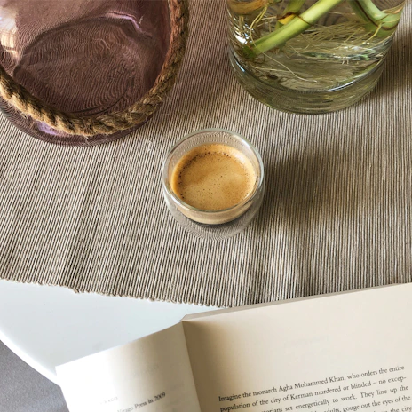 A minimalist espresso cup resting on a textured linen napkin beside an open book.