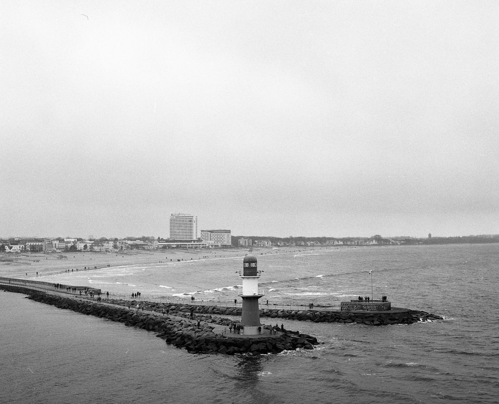 grayscale photo of lighthouse near body of water