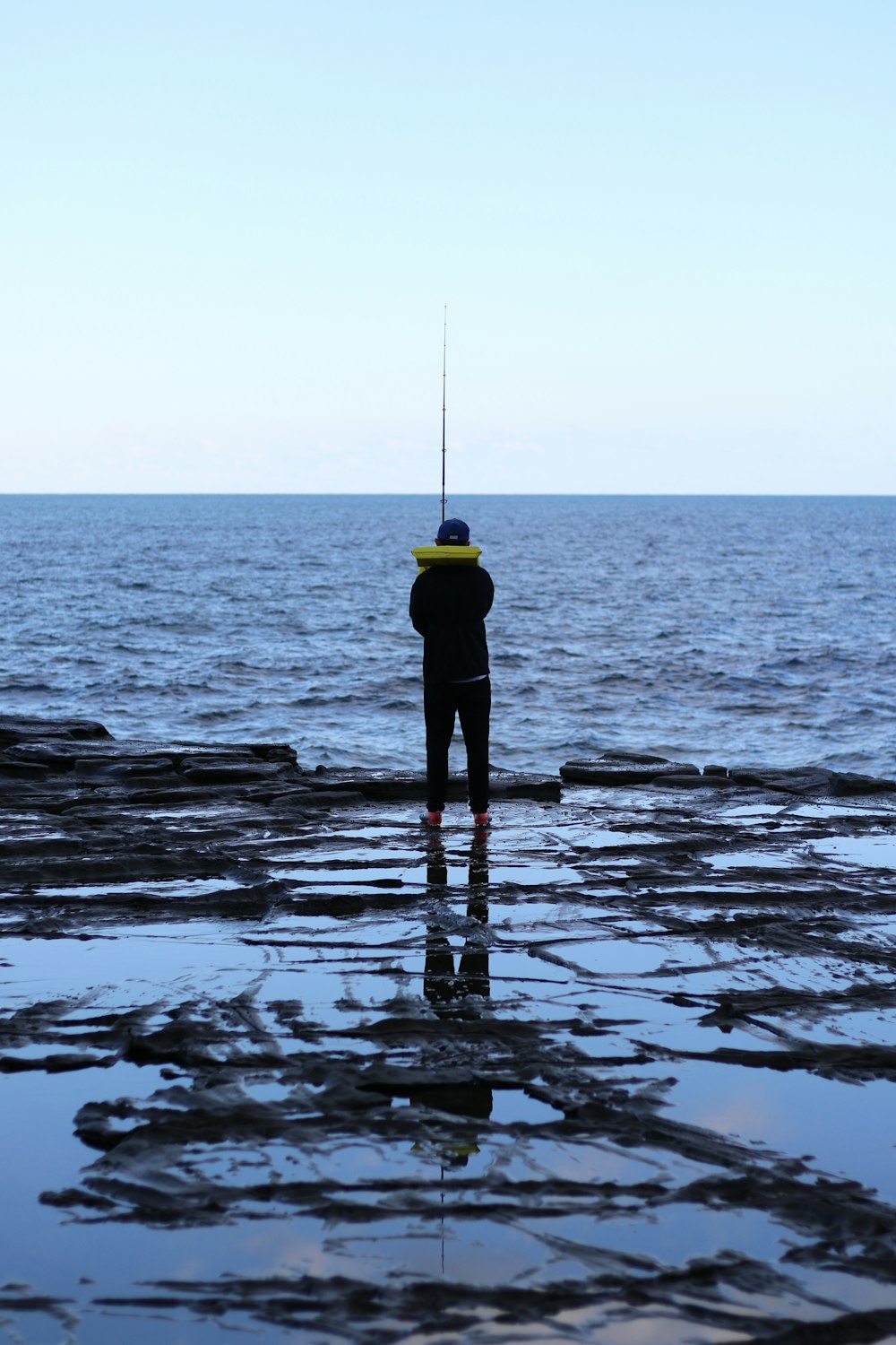 person in yellow jacket standing on rock in the middle of sea during daytime