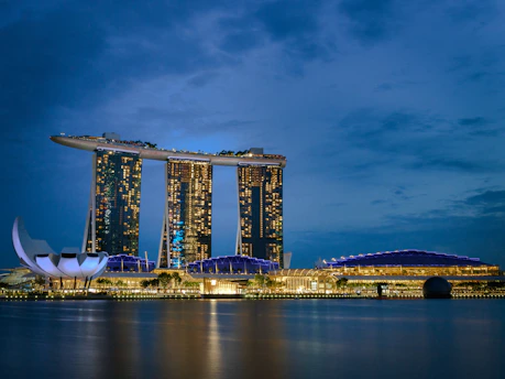 A sleek, modern luxury condominium tower in Singapore glowing warmly at dusk.