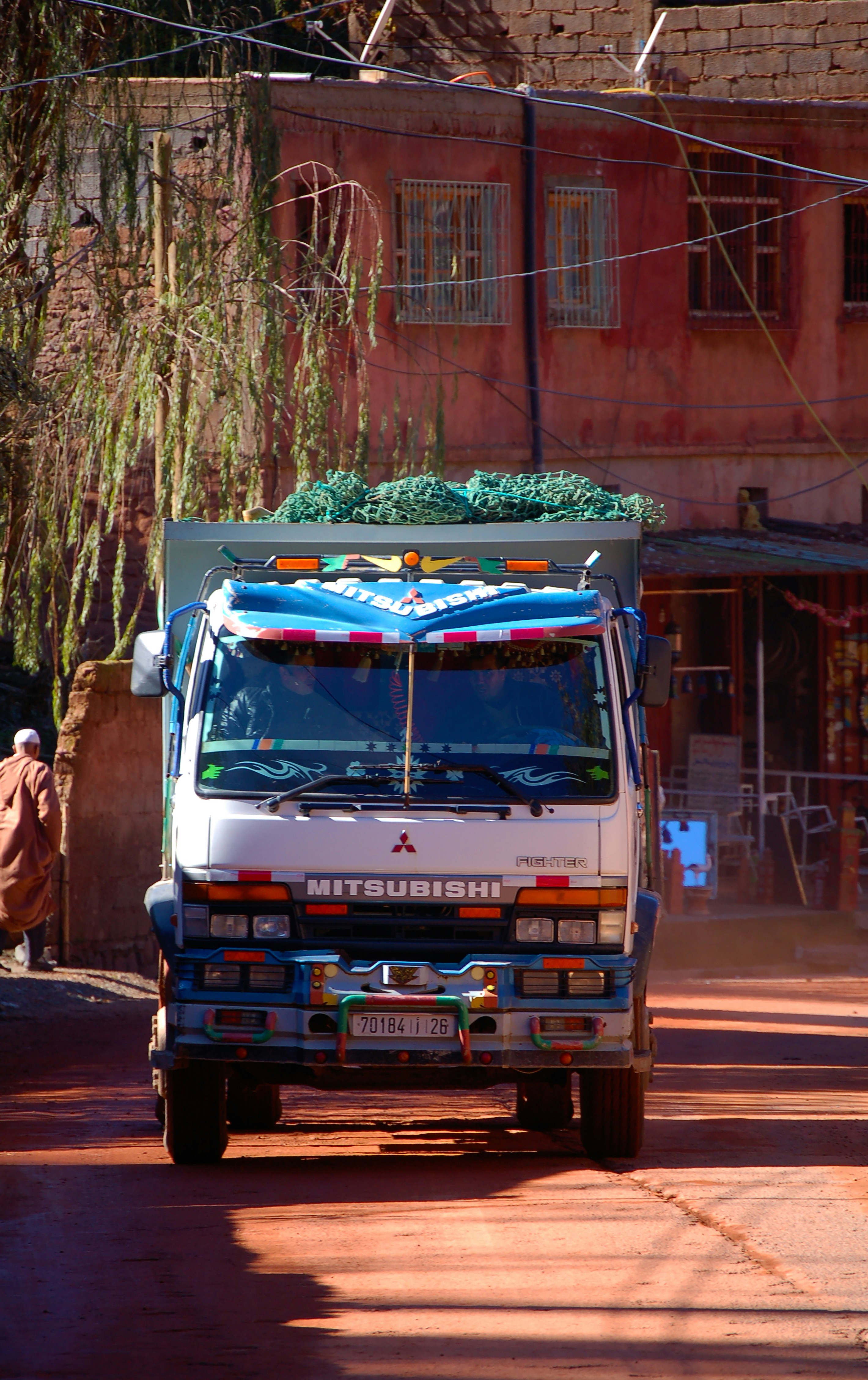man in brown jacket standing beside blue and white truck during daytime