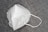 A white KN95 face mask is placed on a textured gray surface. The mask features a simple design with visible stitching and ear loops.