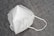 A white KN95 face mask is placed on a textured gray surface. The mask features a simple design with visible stitching and ear loops.