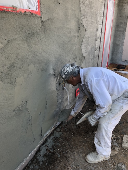 A worker smoothing plaster on a ceiling in a bright room.