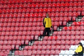 man in yellow polo shirt and black pants standing on red plastic chair