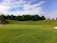 Athletic golfer in navy Pinline Co. trousers lining up a putt on a sunny golf course.