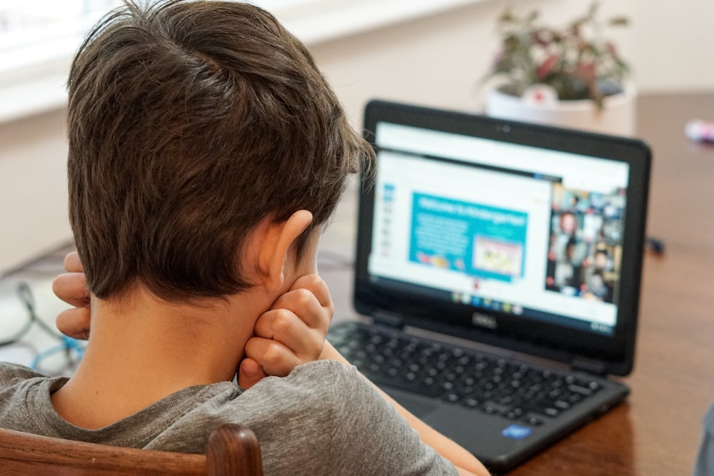 Junge im grauen Hemd mit schwarzem Laptop