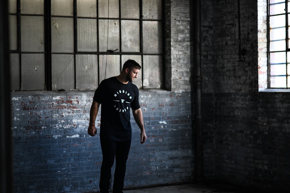 man in black crew neck t-shirt and black pants standing beside gray brick wall