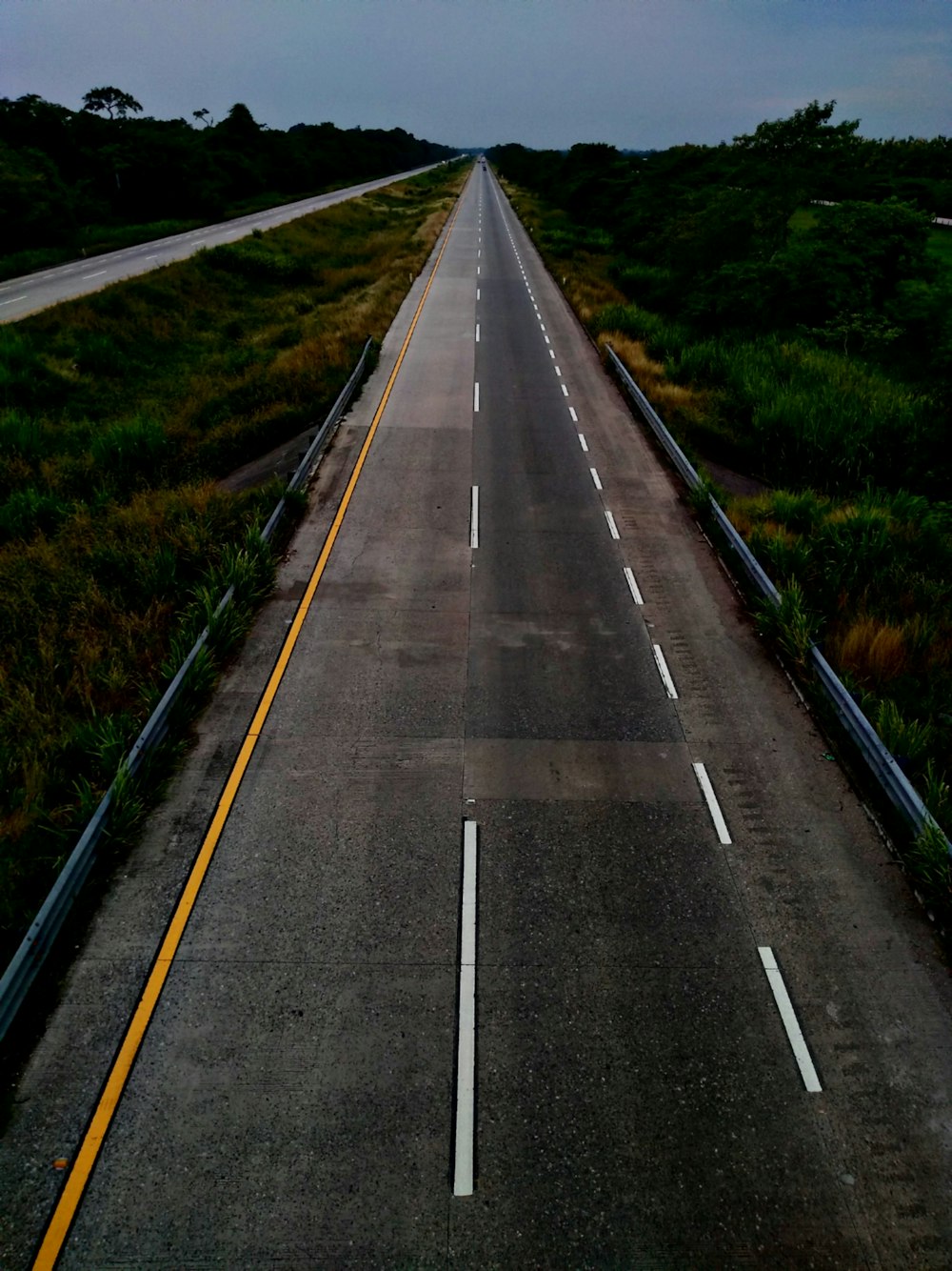 gray concrete road between green grass during daytime