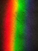 A vivid spectrum of colors appears on a textured surface, with shades transitioning smoothly from red to orange, green, and finally to blue and purple. The colors seem to gently blend into one another, creating a colorful and pleasing visual gradient.