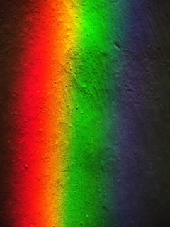 A vivid spectrum of colors appears on a textured surface, with shades transitioning smoothly from red to orange, green, and finally to blue and purple. The colors seem to gently blend into one another, creating a colorful and pleasing visual gradient.
