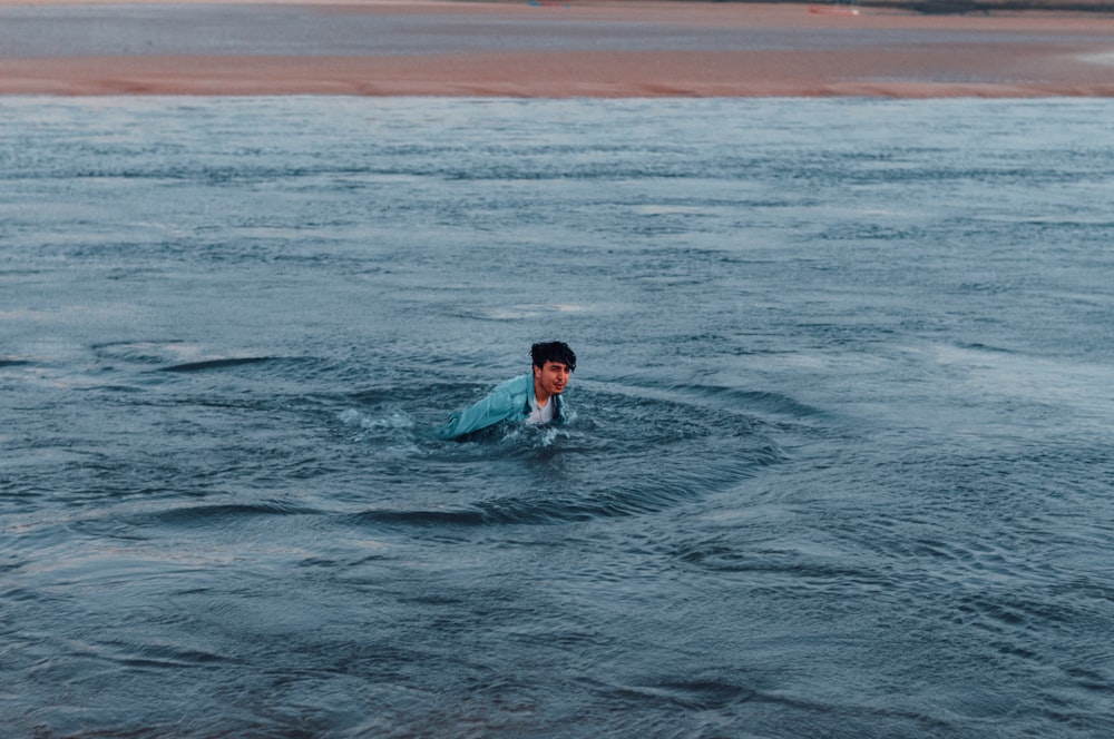 man in blue shirt swimming on sea during daytime