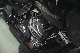 A close-up view of a motorcycle engine featuring polished chrome components and intricate detailing. The Harley-Davidson logo is visible on the side, emphasizing the craftsmanship of the machine.