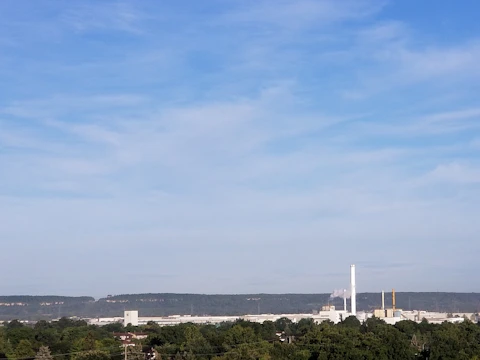 Field researchers measuring noise and emissions near a factory surrounded by greenery.