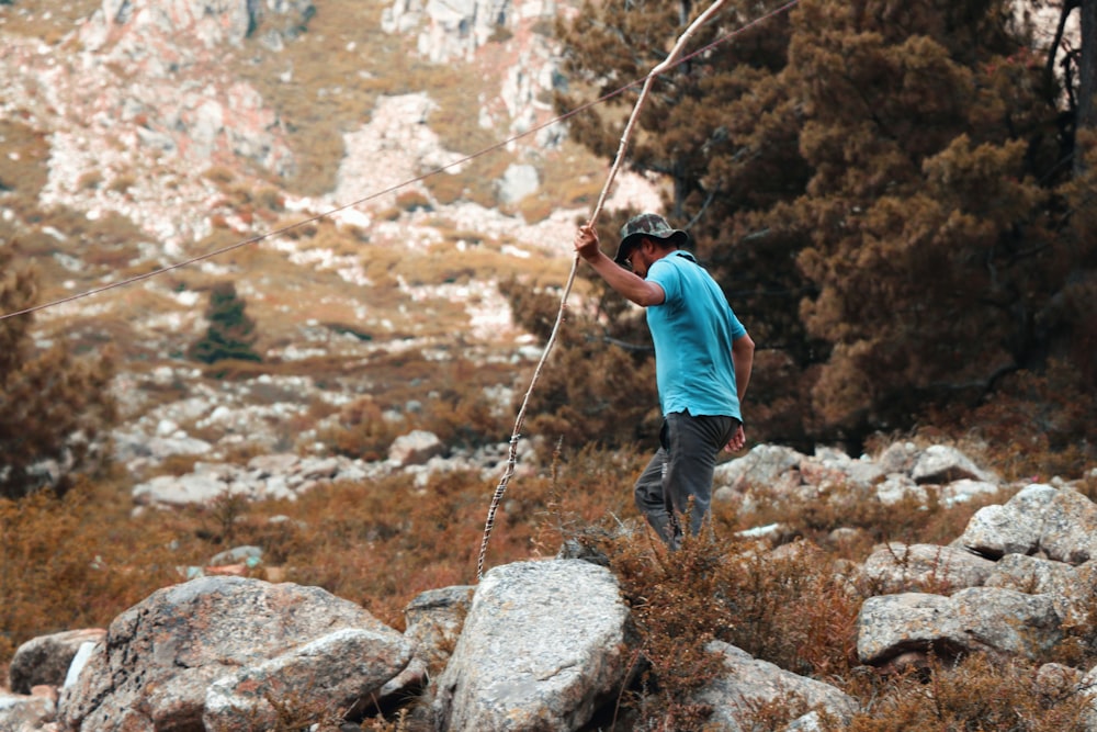 Uomo in maglietta blu e jeans blu denim che si arrampica sulla montagna rocciosa durante il giorno