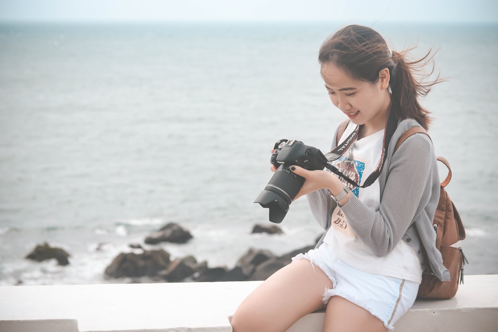 Mujer con camisa blanca de manga larga sosteniendo una cámara DSLR negra