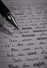 A close-up image of a lined page containing handwritten text with a black pen placed diagonally across it. The text is in cursive script and includes various sentences written in English. The image is in black and white, highlighting the contrast between the ink and the paper.