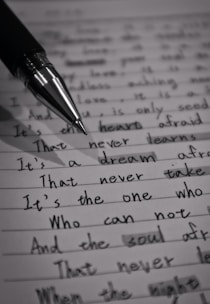 A close-up image of a lined page containing handwritten text with a black pen placed diagonally across it. The text is in cursive script and includes various sentences written in English. The image is in black and white, highlighting the contrast between the ink and the paper.