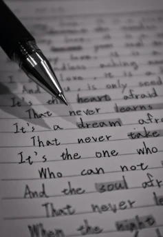 A close-up image of a lined page containing handwritten text with a black pen placed diagonally across it. The text is in cursive script and includes various sentences written in English. The image is in black and white, highlighting the contrast between the ink and the paper.