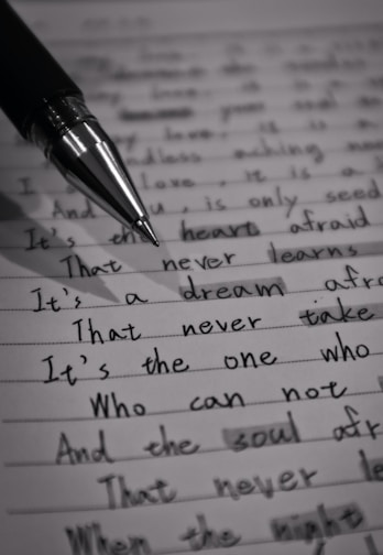 A close-up image of a lined page containing handwritten text with a black pen placed diagonally across it. The text is in cursive script and includes various sentences written in English. The image is in black and white, highlighting the contrast between the ink and the paper.