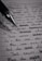A close-up image of a lined page containing handwritten text with a black pen placed diagonally across it. The text is in cursive script and includes various sentences written in English. The image is in black and white, highlighting the contrast between the ink and the paper.