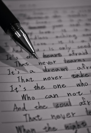 A close-up image of a lined page containing handwritten text with a black pen placed diagonally across it. The text is in cursive script and includes various sentences written in English. The image is in black and white, highlighting the contrast between the ink and the paper.