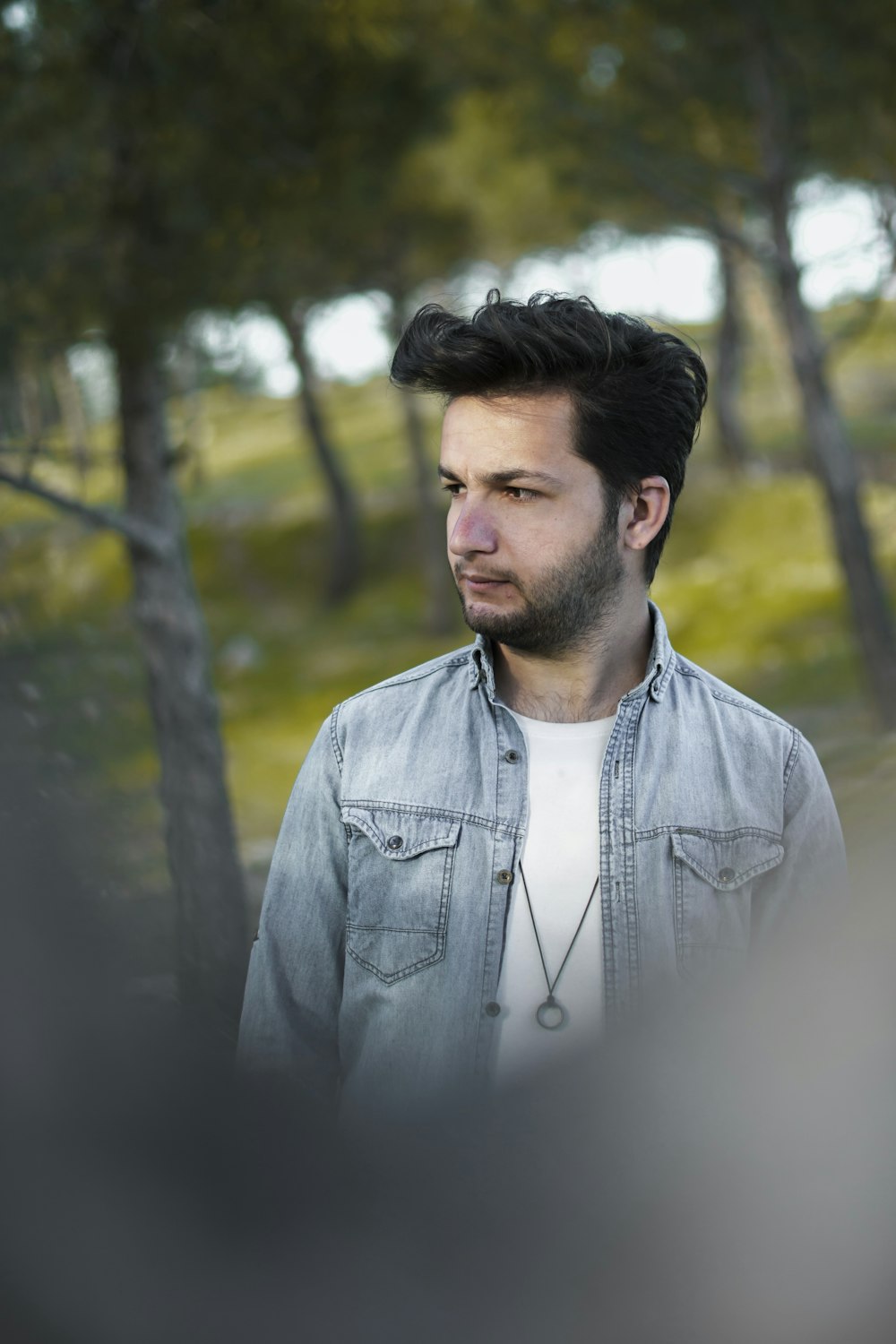 man in gray zip up jacket standing near green trees during daytime