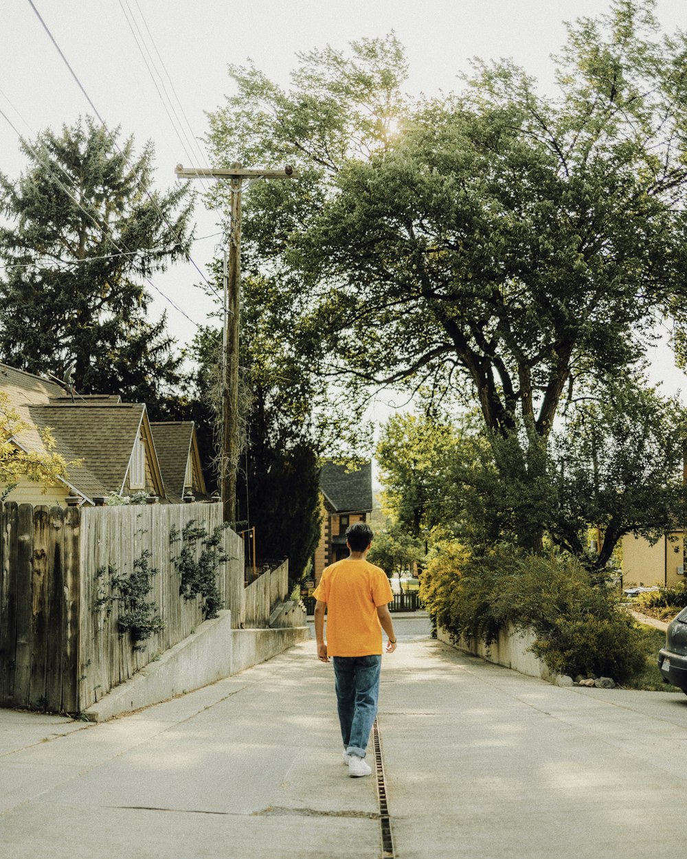 man in orange hoodie walking on sidewalk during daytime