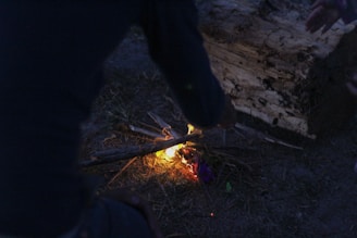 A small campfire glowing softly beside a neatly packed backpack at dusk.