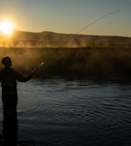 silhouette of man fishing on lake during sunset