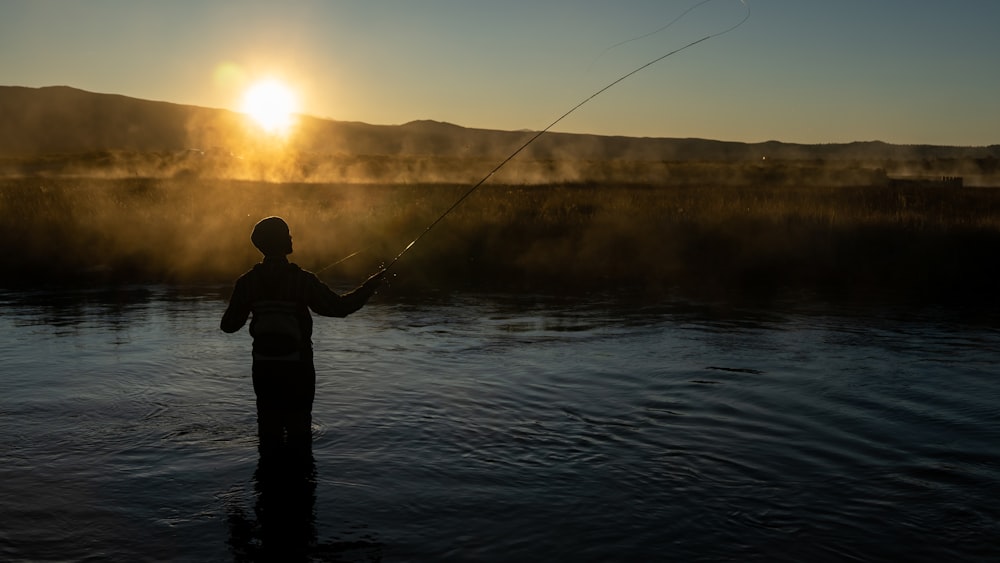 silhouette of man fishing on lake during sunset