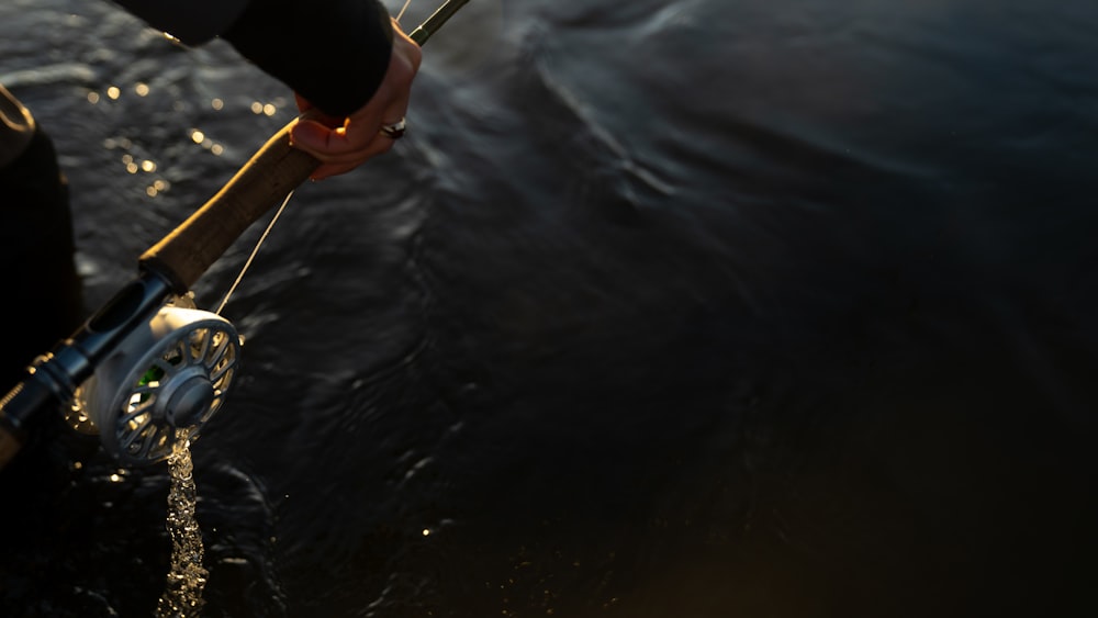 person in black shirt and brown shorts holding brown wooden stick on body of water during