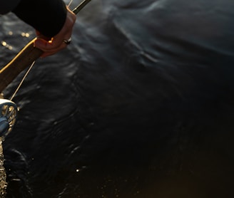 person in black shirt and brown shorts holding brown wooden stick on body of water during