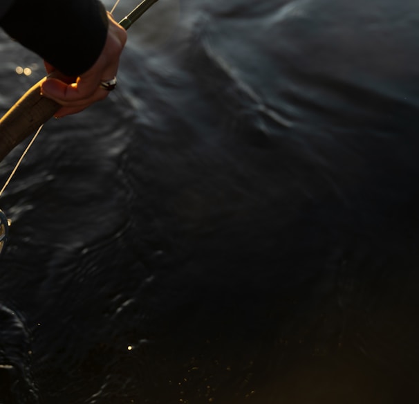 person in black shirt and brown shorts holding brown wooden stick on body of water during